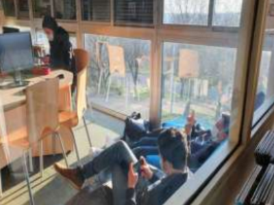 photo du CDI "après" composée d'une élève travaillant dans l'espace "informatique" et de deux élèves lisant sur des poufs près des fenêtres